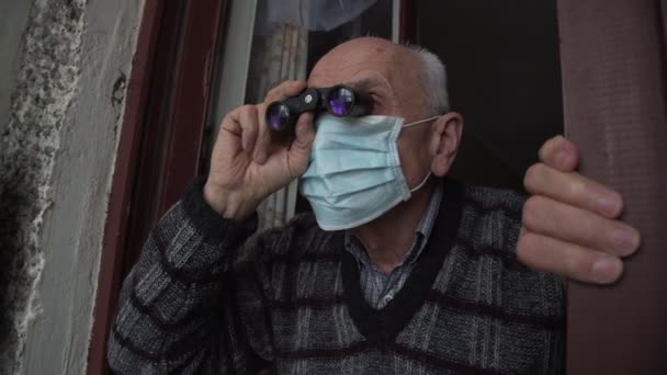 Seltsamer alter Mann mit medizinischer Gesichtsmaske und Fernglas in der Hand — Stockvideo