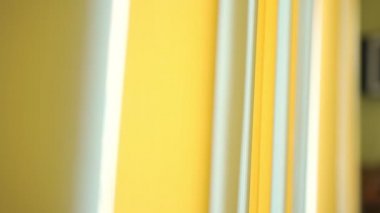 Dikey beyaz ve sarı perdelerin arkaplanı rüzgarla sallanıyor.