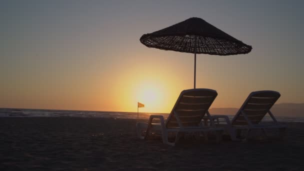 Krásný západ slunce pláž scéna se dvěma židlemi na písečné pláži proti moři. — Stock video