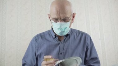 Gözlüklü ve maske takan yetişkin bir adam gazete okuyor.