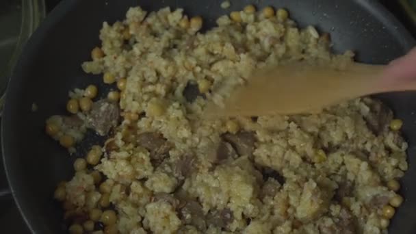 Person bereitet Reis und Fleisch auf Pfanne zu und mixt Mahlzeit mit Holzlöffel. — Stockvideo