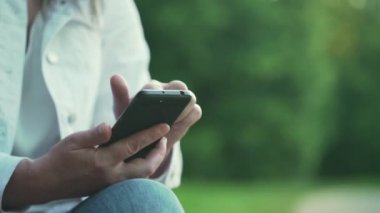 Akıllı telefonlu bir kadın parktaki bankta el ele oturuyor.