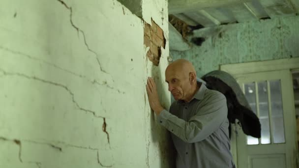 Reifer grauhaariger Mann steht in verlassener Wohnung und berührt Betonwand — Stockvideo