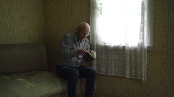 Oude gepensioneerde man met grijs haar en bril opent krant — Stockvideo