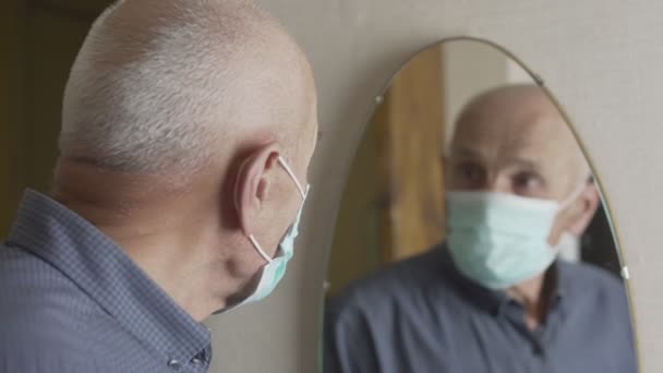 Åldrad man med grått hår ser sig i spegeln och tar av masken — Stockvideo