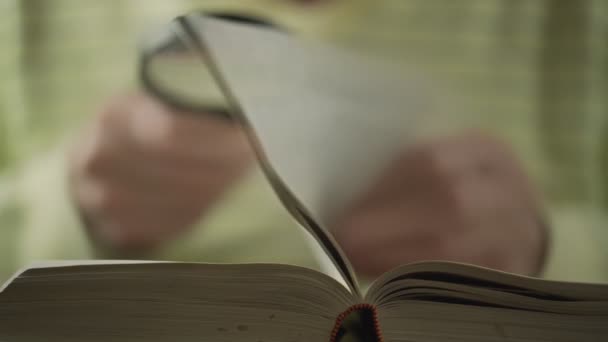 Blurred senior pensioner man in pullover reads large book — Stock Video