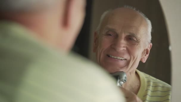 Leende senior man med grått hår rakar med elektrisk rakhyvel — Stockvideo