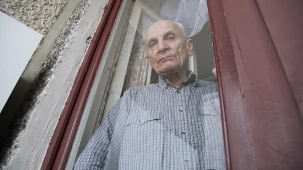 Σοβαρός ηλικιωμένος άντρας κοιτάζει μέσα από ένα ξεπερασμένο παράθυρο. — Αρχείο Βίντεο
