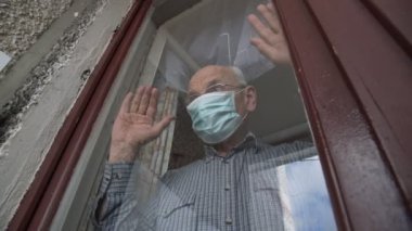 Tek kullanımlık maskeli ve gözlüklü yaşlı adam el sallıyor.