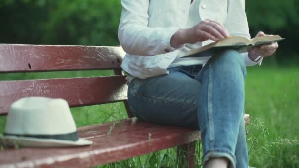Jovem mulher senta-se no banco de madeira vermelho e lê livro — Vídeo de Stock