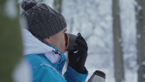 Öreg túrázó sportos dzsekiben forró teát iszik az erdőben — Stock videók