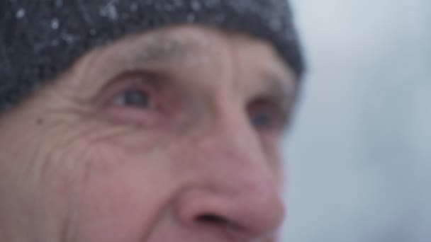 Στοχαστικός γέρος με γκρι καπέλο κοιτάζει τις λευκές νιφάδες χιονιού. — Αρχείο Βίντεο