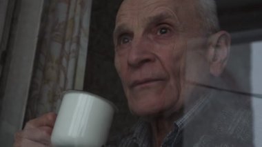 Gri saçlı düşünceli yaşlı adam pencereden dışarı bakıyor.