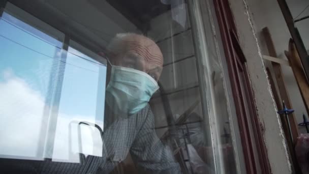 Retired man in blue face mask looks out of old window — Stock Video