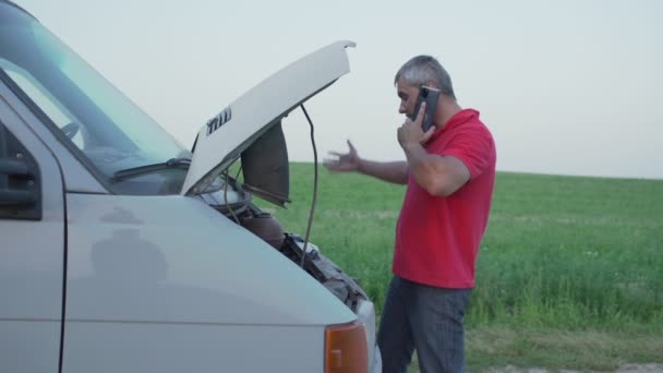 Homem fica perto de carro minivan quebrado com capuz levantado falando por telefone — Vídeo de Stock