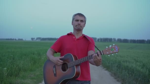 Mand gå i midten af snavs vej på banen og spille på akustisk guitar – Stock-video