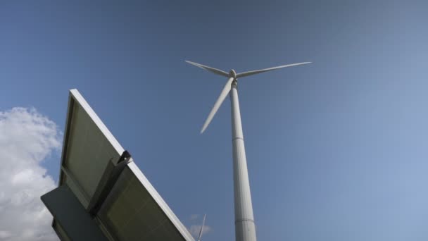 Ветряная мельница и солнечная панель для производства энергии под голубым небом — стоковое видео