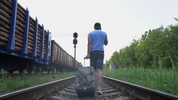 Людина з мішком ходить по залізниці біля проїзду поїзда і розмовляє по телефону — стокове відео