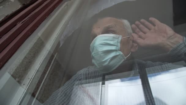 Pensionista sênior emocional em máscara facial coloca as mãos na janela — Vídeo de Stock