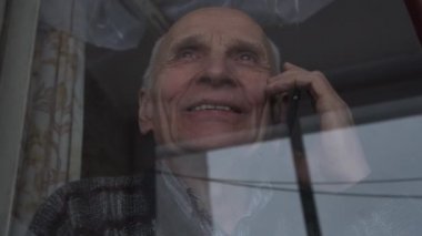 Kırışıklıkları olan neşeli yaşlı adam akıllı telefondan konuşuyor.