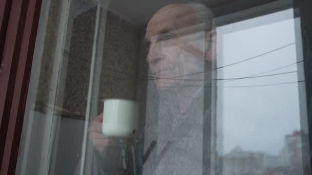 Hombre viejo silueta mira fuera de la ventana grande y sostiene taza — Vídeo de stock