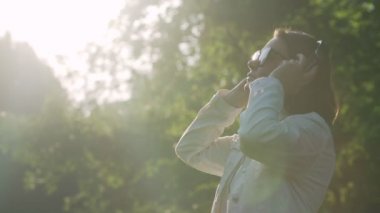 Güneş gözlüklü ve kulaklıklı genç kadın müzik dinliyor.