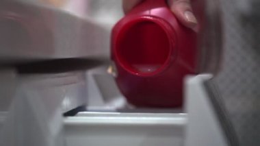 Genç bir kadın çamaşır makinesine beyaz sıvı sabun döküyor.