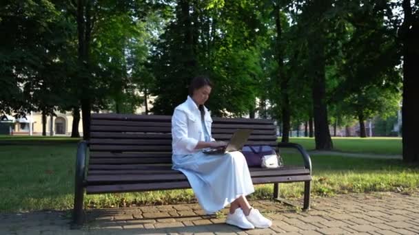 Brunette woman in white clothes works on notebook in park — Stock Video