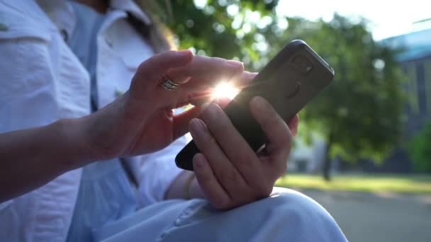 Mujer de chaqueta blanca lee mensajes en el teléfono inteligente en el parque — Vídeo de stock