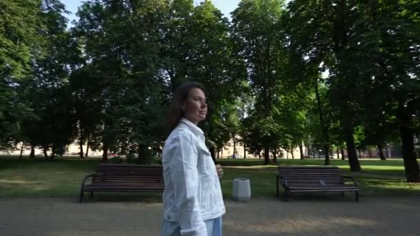 Middelbare vrouw loopt langs park schaduw steeg met laptop tas — Stockvideo