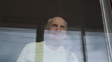 Yaşlı, gri saçlı, emekli adam pencereden bakıyor.
