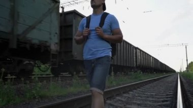 Sırt çantalı bir adam tren rayları boyunca yürüyor.