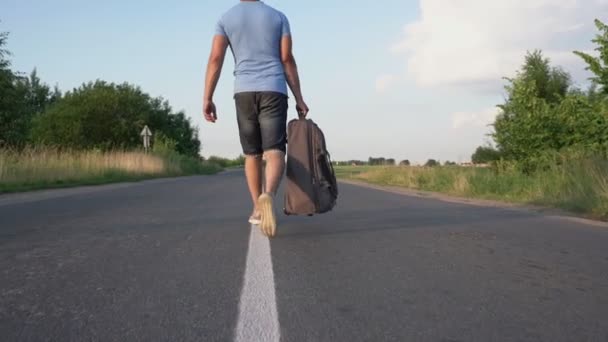 Man buiten de stad loopt in het centrum van de weg en draagt road bag achteraanzicht — Stockvideo