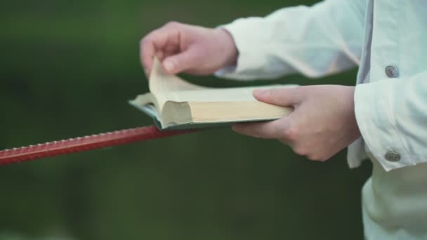 Young woman reader turns small book pages holding on fence — Stock Video