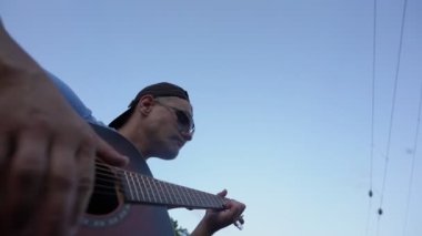 Güneş gözlüğü takan ve gitar çalan bir müzisyen.