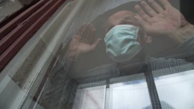 Mavi maskeli yaşlı adam pencereden bakıyor.