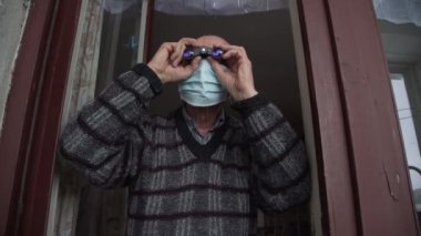 Yüz maskeli tuhaf yaşlı adam siyah dürbünle izliyor.