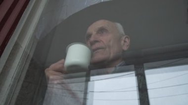 Kırışıklıkları olan yaşlı bir adam sıcak bir içeceğin tadına bakar.