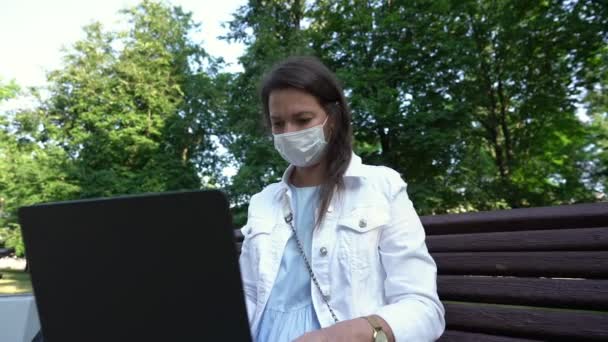 Vrouw in wegwerp masker types brief op laptop in park — Stockvideo