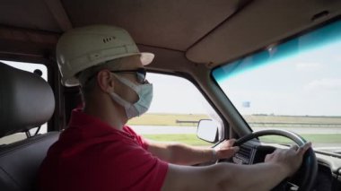 Beyaz miğfer ve tıbbi maske takan yetişkin bir sürücü kamyonda..