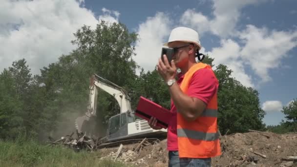 Man ingenieur dragen helm en vest praten via de telefoon op de bouwplaats — Stockvideo