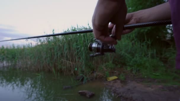 Visser houdt vishengel met zijn handen en draait vissen haspel op meer — Stockvideo