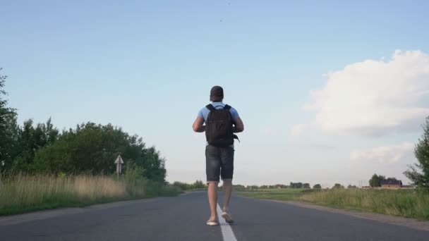 Man met rugzak wandelen buiten de stad in het centrum van de weg achteraanzicht — Stockvideo