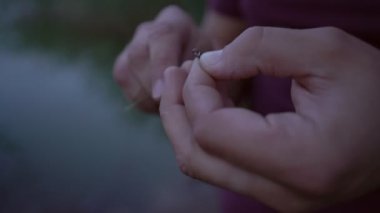 Parmakları olan bir balıkçı misinayı karabina deliğine geçirir.