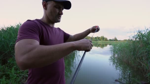 Człowiek rybak rozpakowuje wędkę na brzegu małego stawu — Wideo stockowe