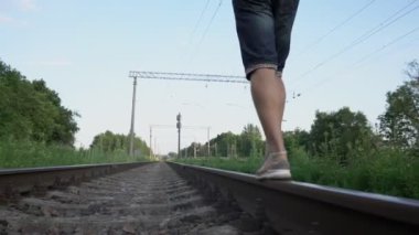 Sırt çantalı bir adam demiryolunda yürüyor.