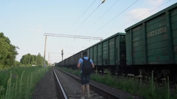 Человек ходит по рельсам железной дороги, не обращая внимания на проходящий поезд — стоковое видео
