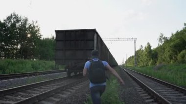 Sırt çantalı bir adam giden trenin arkasında koşuyor ve elini sallıyor.