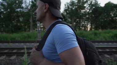 Sırt çantalı erkek gezgin demiryolu raylarının yanından geçiyor ve uzaklaşıyor.
