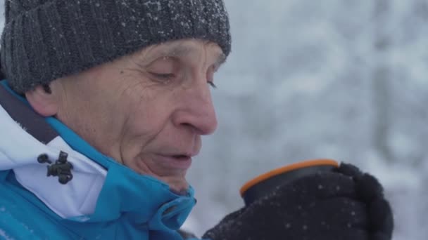 Homem idoso esportivo admira queda de neve segurando copo térmica chá — Vídeo de Stock